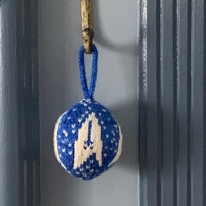 May include: A blue and white knitted Christmas bauble with a white snowflake design hanging from a hook.