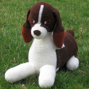 May include: A crocheted stuffed dog toy with brown and white fur. The dog is sitting on its hind legs with its front legs outstretched.