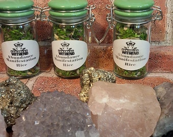 May include: Three small glass jars with green lids filled with rice and herbs. Each jar has a white label with the text "Healing Within" and "Abundance Manifestation Rice". The jars are sitting on a surface with various crystals.