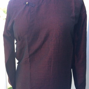 May include: A long-sleeved burgundy shirt with a mandarin collar and gold buttons. The shirt has a subtle sheen and a textured fabric.