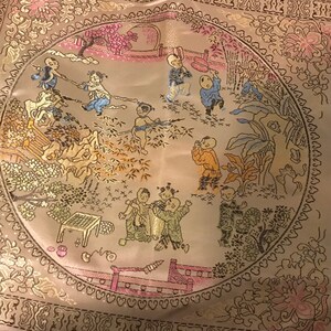 May include: A circular embroidered fabric panel with a beige background and a gold border. The panel features a scene of children playing in a garden with trees, flowers, and a bridge. The children are wearing traditional Chinese clothing.