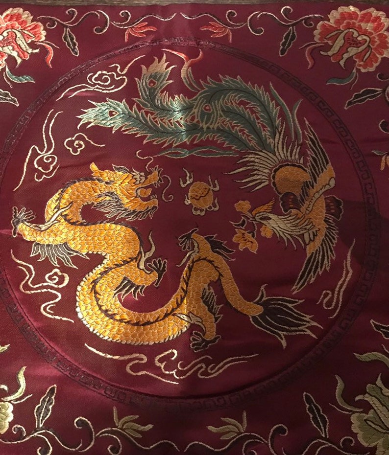 May include: A red silk cushion with a gold embroidered dragon and phoenix design. The cushion has a circular design with a border of gold and black.
