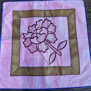 K&ouml;nnte beinhalten: Ein rosa Kissen mit einem goldenen und braunen bestickten Rand und einem rosa Blumendesign in der Mitte.