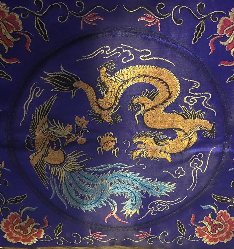 May include: A purple silk cushion with a gold and blue embroidered design of a dragon and a phoenix. The cushion is decorated with floral motifs and clouds.