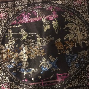 May include: A black circular cushion with a gold and silver embroidered design of people and plants. The design is in a circle with a border of gold and silver.