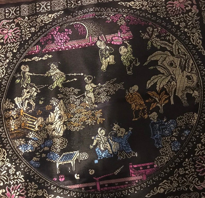 May include: A black circular cushion with a gold and silver embroidered design of people and plants. The design is in a circle with a border of gold and silver.