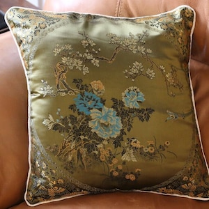 May include: A green throw pillow with a white border features an embroidered design of blue flowers and branches with gold accents.