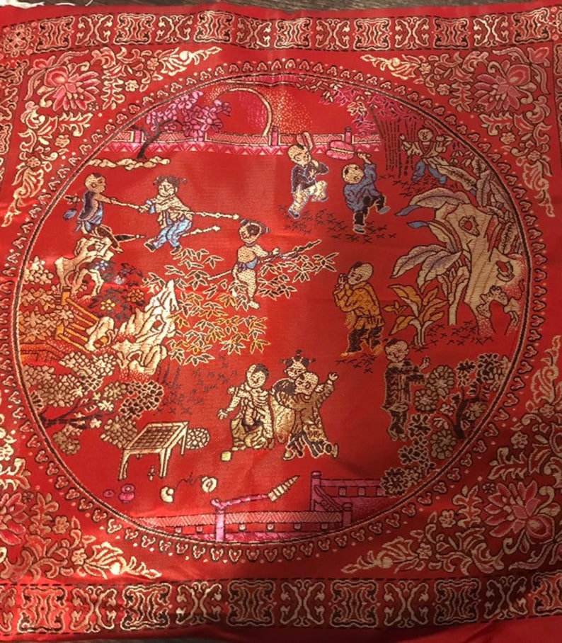 May include: A red square cushion with a gold embroidered border and a circular design of children playing in a garden. The design includes trees, flowers, and a fence.