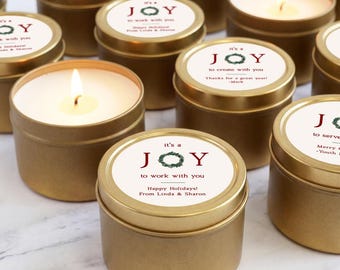 May include: A collection of round gold metal candle tins with white circular labels. Each label features the text 'it's a JOY to work with you' or similar variations, a green wreath graphic, and personalized holiday messages from various senders.