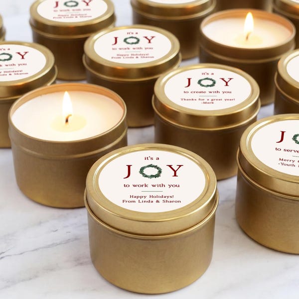 May include: A collection of round gold metal candle tins with white circular labels. Each label features the text 'it's a JOY to work with you' or similar variations, a green wreath graphic, and personalized holiday messages from various senders.
