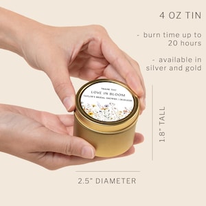 May include: A gold-colored 4 oz metal candle tin with a 2.5-inch diameter and 1.8-inch height. The lid features a label with a floral illustration and the text: THANK YOU LOVE IN BLOOM TAYLOR'S BRIDAL SHOWER | 08.29.2026. It has a 20-hour burn time.