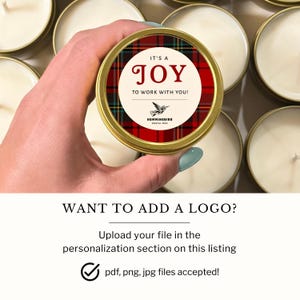 May include: A round gold metal candle tin with a red, green, and black plaid label. The label features a cream-colored center circle with the text IT'S A JOY TO WORK WITH YOU! and a small hummingbird icon above the text HUMMINGBIRD DIGITAL TECH.