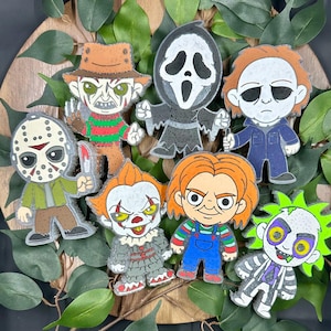 May include: A collection of cartoon-style horror movie character pins, including Freddy Krueger, Ghostface, Michael Myers, Jason Voorhees, Pennywise, Chucky, and Beetlejuice. Each pin features vibrant colors and detailed designs, perfect for fans of the horror genre.