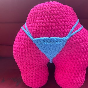 Peut inclure: Un grand coussin rose fait &agrave; la main en crochet en forme de fesses, avec un bikini bleu clair en crochet. Le coussin est fait de fil &eacute;pais et textur&eacute;. Le bikini a de fines bretelles et un devant triangulaire.