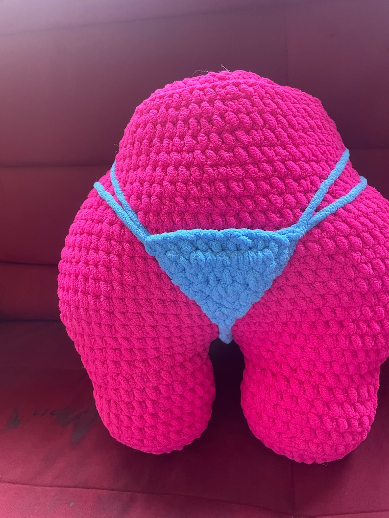 Peut inclure: Un grand coussin rose fait &agrave; la main en crochet en forme de fesses, avec un bikini bleu clair en crochet. Le coussin est fait de fil &eacute;pais et textur&eacute;. Le bikini a de fines bretelles et un devant triangulaire.