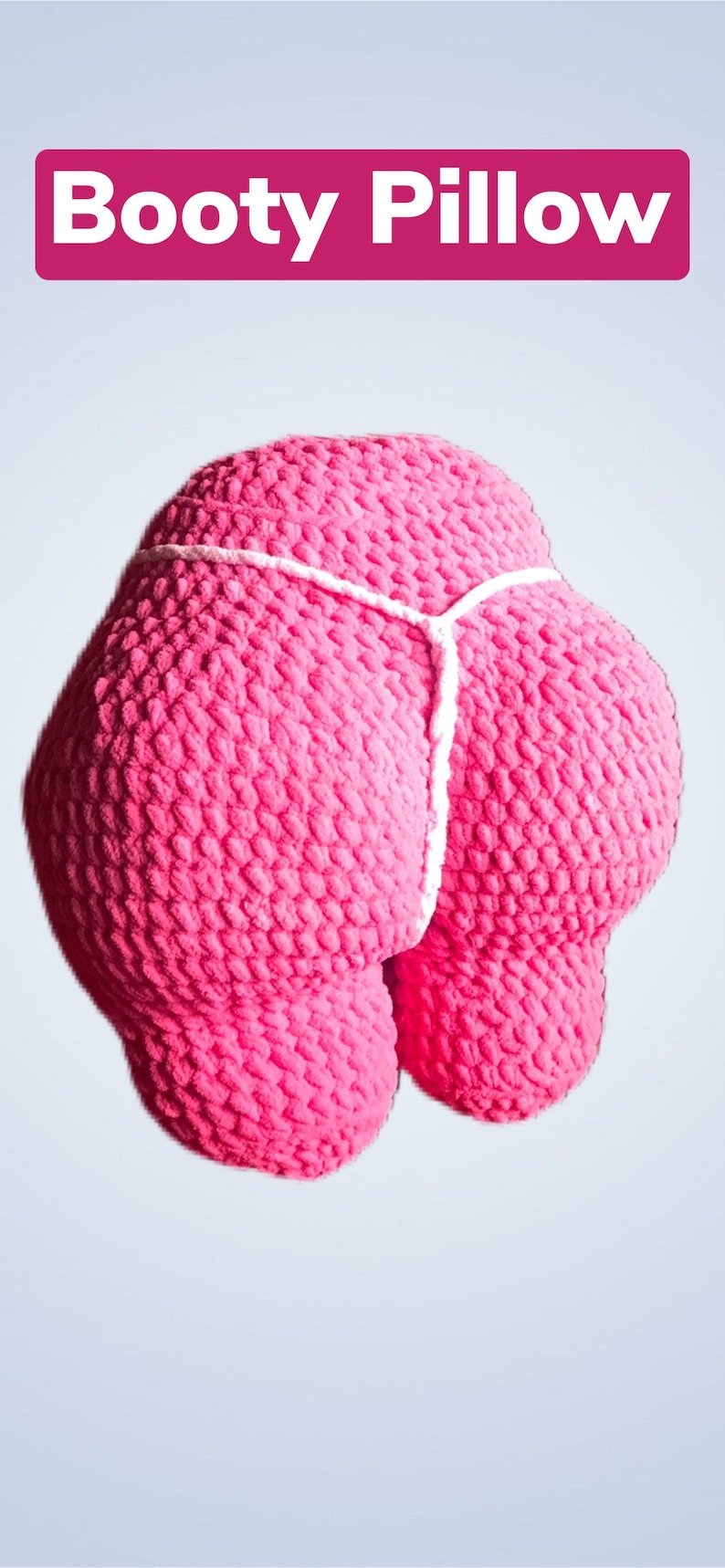 Peut inclure: Un coussin rose en crochet en forme de fesses, avec un d&eacute;tail de ficelle blanche. Le texte "Booty Pillow" est affich&eacute; dans un rectangle rose en haut de l'image. L'oreiller est un article fantaisie.