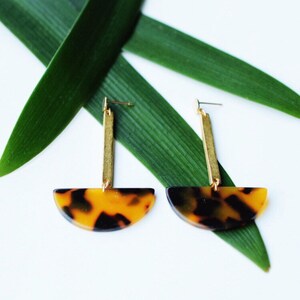 May include: A pair of gold and tortoiseshell earrings. The earrings feature a long gold bar with a half-circle tortoiseshell pendant.