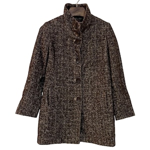 May include: A brown and white tweed coat with a high collar and large brown buttons. The coat has long sleeves and two front pockets. The coat is hanging on a hanger.
