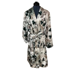 May include: A long, floral-patterned robe in shades of white, gray, and green, tied at the waist with a matching belt. The robe is displayed on a mannequin, showcasing its flowing design and long sleeves. The floral pattern adds a touch of elegance.