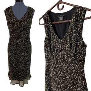 May include: A sleeveless black dress with a V-neck and a subtle pattern of small, light-colored dots. The dress has a fitted bodice and a slightly flared skirt with a sheer, ruffled hem. The dress is displayed on a mannequin and a hanger.