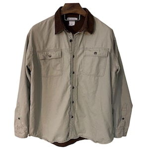 May include: A tan Columbia button-up shirt with a brown corduroy collar. The shirt has two chest pockets, buttoned cuffs, and a brown lining at the bottom. The Columbia logo is visible on the chest pocket.