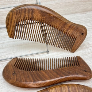 May include: Three wooden combs with a curved shape and brown wood grain. The combs are made of dark brown wood and have a natural finish.