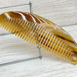 May include: A brown and yellow tortoiseshell comb with a curved handle and fine teeth.