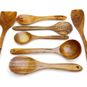 May include: A set of seven wooden kitchen utensils featuring a variety of spoons, a slotted spoon, a fork, and spatulas. Each piece displays a natural brown wood grain pattern and includes a small circular hole at the end of the handle for hanging.