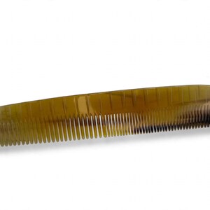 May include: A rectangular hair comb featuring a translucent, mottled amber and brown horn-like pattern. The comb has a series of fine, evenly spaced teeth along one edge and a smooth, slightly curved spine, showcasing natural color variations.