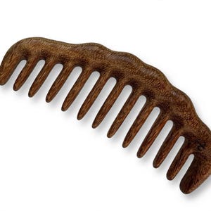 May include: A wide-tooth hair comb crafted from dark brown wood with a visible natural grain pattern. The comb features a curved, ergonomic top edge with a series of eleven sturdy, rounded teeth designed for detangling hair with ease.