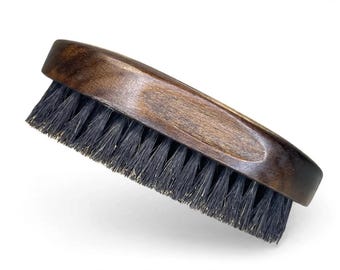 Può includere: Una spazzola da toelettatura di forma ovale con un manico in legno marrone scuro con venature visibili e setole nere dense e rigide. La spazzola presenta un design ergonomico curvo che si adatta comodamente alla mano per l'uso quotidiano.
