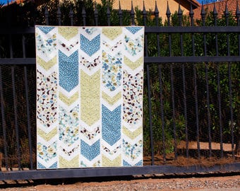 Puede incluir: Una colcha con un patrón de chevron en tonos de azul, amarillo y blanco. La colcha presenta una tela de estampado floral con flores blancas sobre un fondo oscuro.