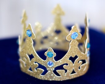 May include: A gold crown with blue gems, on a blue velvet background.