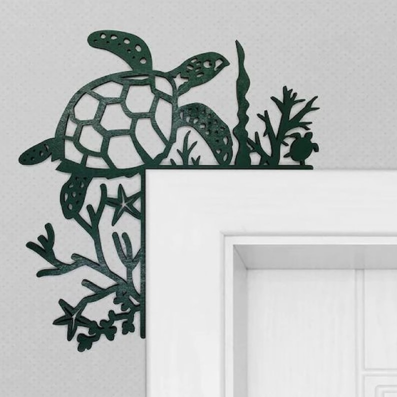 May include: A dark green metal wall decor featuring a sea turtle with seaweed and coral. The turtle is in the upper left corner of the image, and the seaweed and coral are in the lower right corner. The decor is attached to a white door frame.