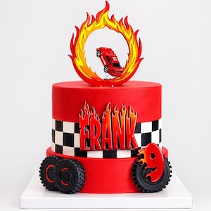 May include: A red birthday cake with a race car theme. The cake features a red car jumping through a flame ring, the name "FRANK" in fiery letters, and a checkered flag design. Black tires and a number 9 complete the design.