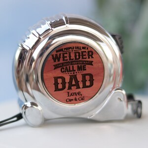 May include: A silver tape measure with a wooden insert that reads "Some people call me a Welder. The most important call me Dad. Love, Cam & Cal."