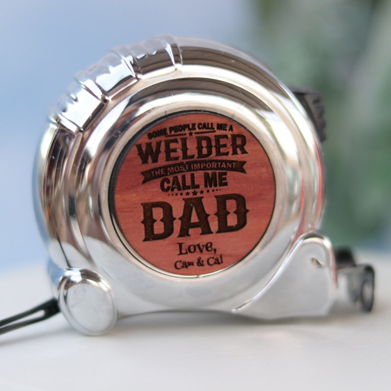 May include: A silver tape measure with a wooden insert that reads "Some people call me a Welder. The most important call me Dad. Love, Cam & Cal."