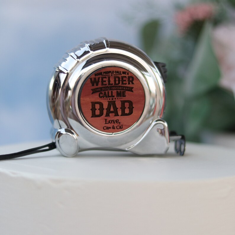 May include: A silver measuring tape with a wooden insert that reads "Some people call me a welder, the most important call me Dad. Love, Cap & Cal."