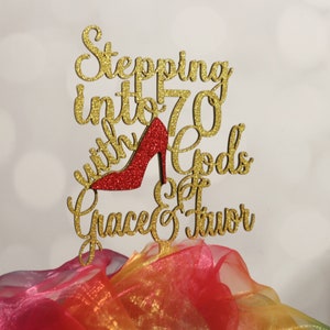 May include: Gold glitter cake topper with the text "Stepping into 70 with Gods Grace & Favor" and a red glitter high heel shoe.