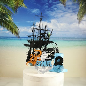 May include: A black silhouette of a pirate ship with a skull and crossbones, an octopus, an anchor, and the name "Samuel" on a cake topper. The cake topper is on a white cake with a blue number 8.