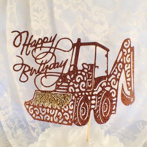 May include: A brown glitter cake topper with the words "Happy Birthday" and a silhouette of a construction excavator.