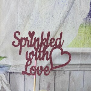 May include: Pink glitter cake topper with the text "Sprinkled with Love" and a heart shape.
