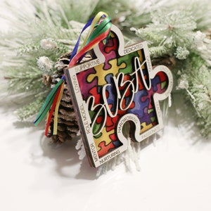 May include: A wooden jigsaw piece ornament with the word "BOBT" in a colourful, stylised font. The jigsaw piece is decorated with a colourful jigsaw pattern and has words like "loving", "supportive", "role model", "mentor", "nurturing", "hardworking", "passionate", "leader", "caring", "dedicated", and "understanding" around the edge.