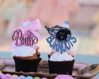 May include: Two cupcakes decorated with pink and blue glitter toppers. The pink topper says "Boos" and the blue topper says "Burnouts".