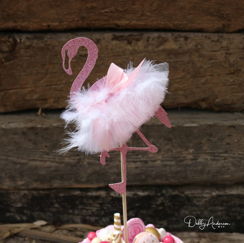 K&ouml;nnte beinhalten: Rosa glitzernder Flamingo-Kuchentopper mit einem wei&szlig;en T&uuml;ll- und Federnrock und einer rosa Schleife.