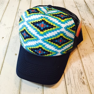 May include: A navy blue trucker hat with a white, blue, yellow, red and black geometric pattern on the front.