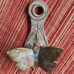 May include: An antique metal wall sconce with a butterfly design. The butterfly has blue and brown wings with yellow accents. The sconce has a decorative top with a circular opening and a detailed, leaf-like base.