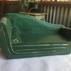 May include: A green wooden chaise lounge with gold trim. The chaise lounge is a miniature version of a full-sized chaise lounge.