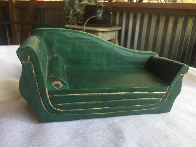 May include: A green wooden chaise lounge with gold trim. The chaise lounge is a miniature version of a full-sized chaise lounge.