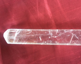 May include: A clear, long, rectangular crystal with a pointed end. The crystal has a smooth, polished surface with visible internal lines.